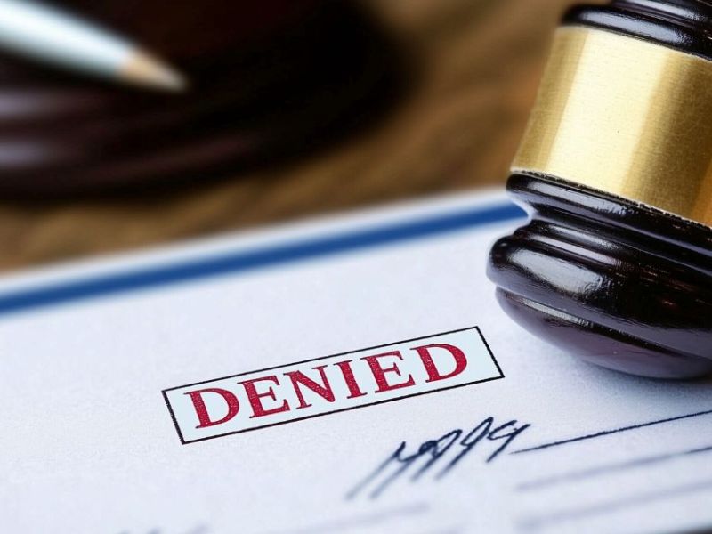 A gavel rests on a document with the bold red word "DENIED" prominently displayed. The scene is set on a wooden surface, suggesting a legal or judicial context.