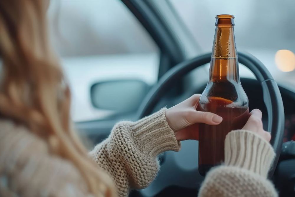 A person holds a bottle while driving, gripping the steering wheel with one hand. The environment suggests a vehicle interior, with blurred lights in the background indicating movement.