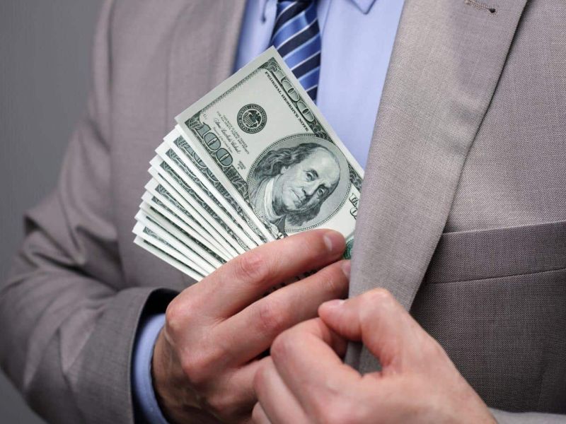 man putting stack of one hundred dollar bills into his suit jacket pocket