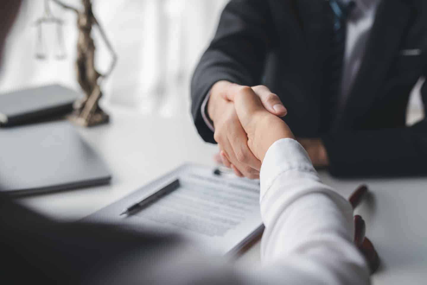 two people shaking hands over a desk with documents in view